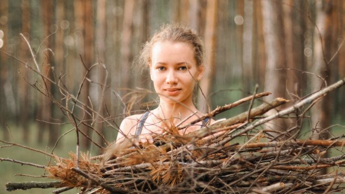 teenage girl with pimple skin collect branches firewood for a campfire while traveling through a summer forest in nature. young happy people survivalist traveler and local travel on great outdoors